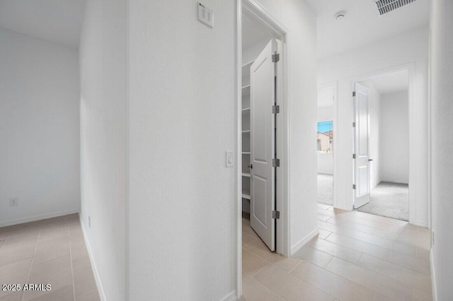 corridor featuring visible vents, baseboards, and light tile patterned flooring