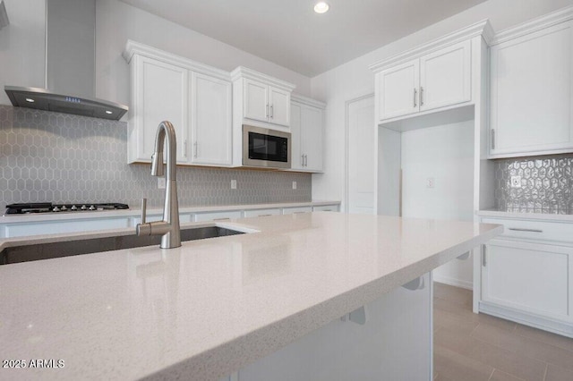 kitchen featuring built in microwave, a sink, white cabinets, wall chimney range hood, and decorative backsplash