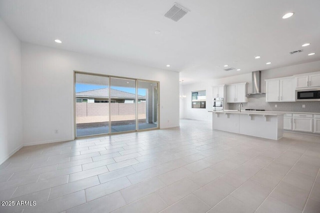 kitchen featuring visible vents, white cabinets, open floor plan, light countertops, and wall chimney range hood