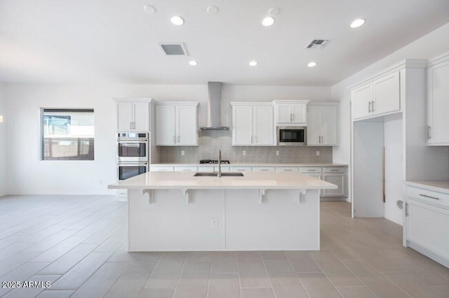 kitchen featuring light countertops, wall chimney range hood, a center island with sink, and built in microwave