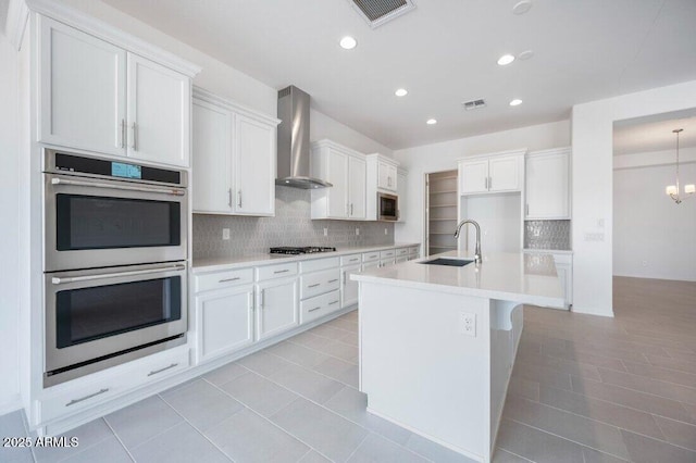 kitchen featuring stainless steel appliances, wall chimney range hood, light countertops, and visible vents