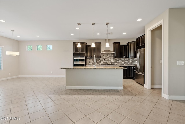 kitchen with decorative backsplash, wall chimney exhaust hood, hanging light fixtures, a kitchen island with sink, and appliances with stainless steel finishes