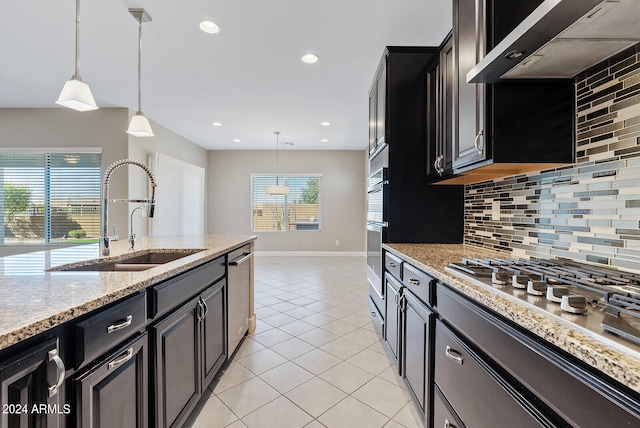 kitchen featuring backsplash, decorative light fixtures, wall chimney range hood, and sink