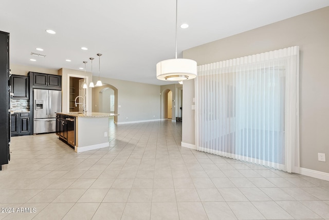 kitchen featuring stainless steel appliances, light stone countertops, a kitchen island with sink, pendant lighting, and light tile patterned floors