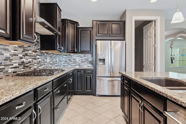 kitchen with backsplash, light stone countertops, stainless steel appliances, pendant lighting, and wall chimney range hood