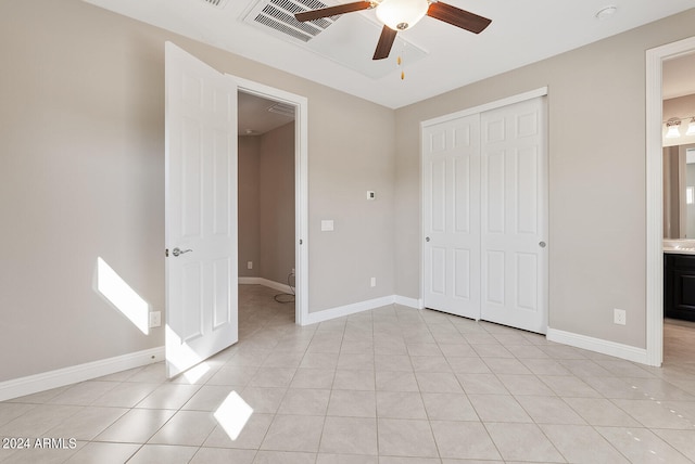 unfurnished bedroom with a closet, ceiling fan, light tile patterned floors, and ensuite bath