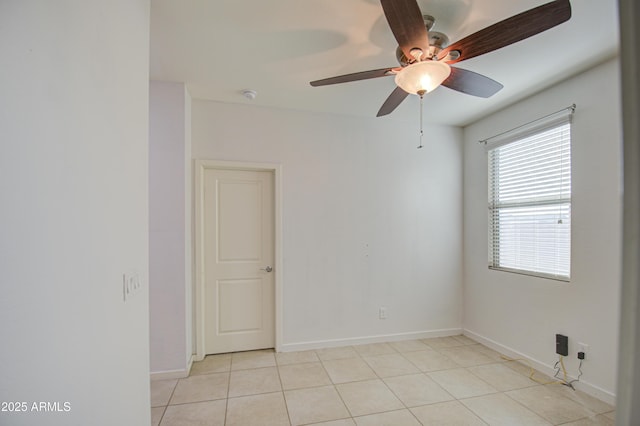 empty room featuring light tile patterned floors, a ceiling fan, and baseboards