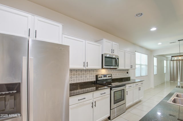 kitchen with stainless steel appliances, decorative backsplash, white cabinets, light tile patterned flooring, and dark stone countertops