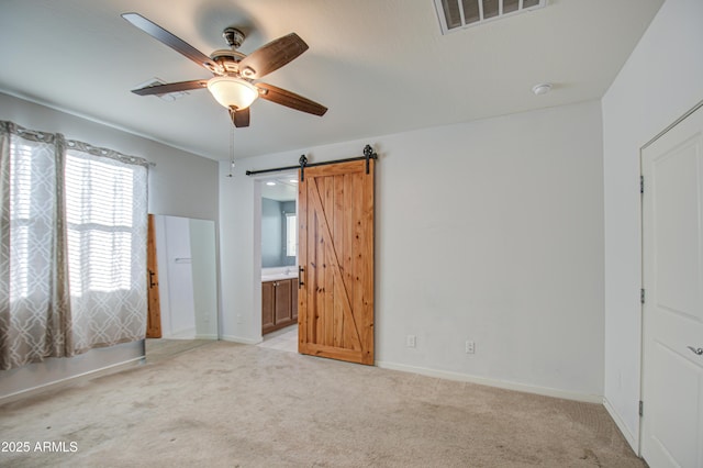 unfurnished bedroom with a barn door, visible vents, baseboards, light colored carpet, and ensuite bath