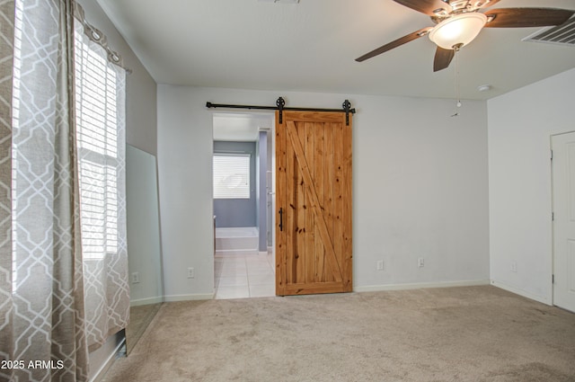 empty room with carpet floors, a barn door, a ceiling fan, and baseboards