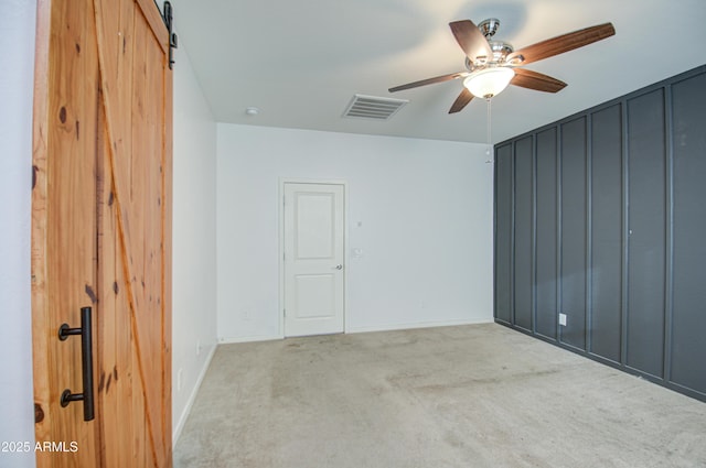 carpeted spare room with ceiling fan, a barn door, visible vents, and baseboards