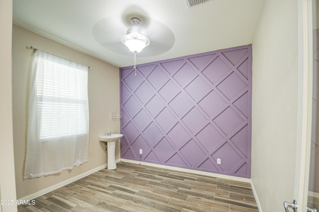 unfurnished room featuring wood finish floors, an accent wall, a sink, ceiling fan, and baseboards