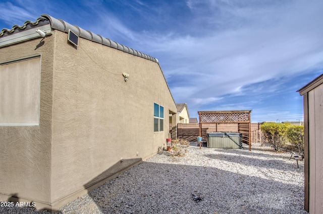 view of side of property with stucco siding, a fenced backyard, and a hot tub