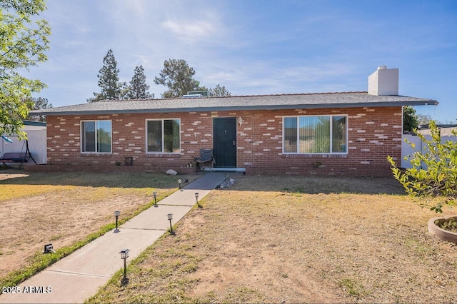 single story home with brick siding, a chimney, and a front yard
