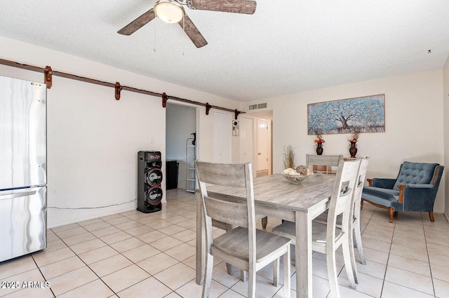 dining area with a barn door, light tile patterned floors, a ceiling fan, and a textured ceiling