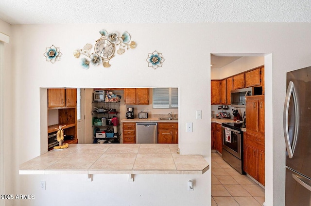 kitchen featuring stainless steel appliances, a sink, brown cabinetry, light countertops, and a textured ceiling