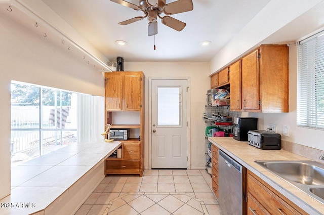 kitchen featuring dishwasher, a sink, light tile patterned flooring, a ceiling fan, and brown cabinetry