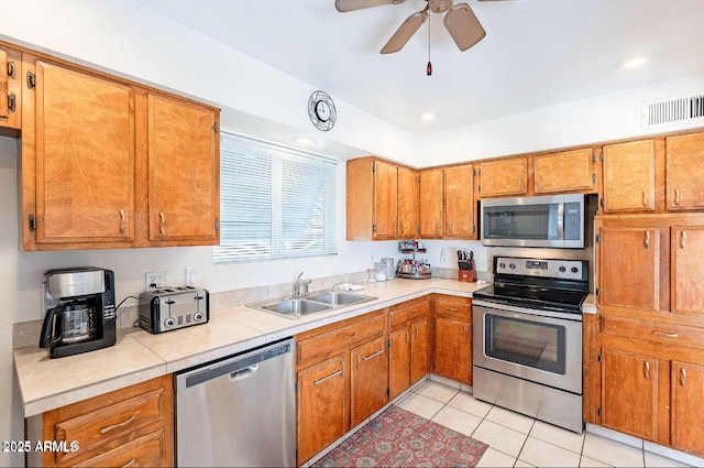 kitchen with appliances with stainless steel finishes, a sink, brown cabinets, light tile patterned floors, and ceiling fan