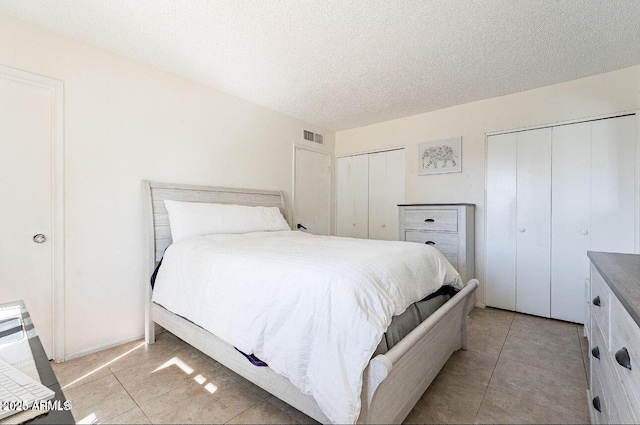 bedroom featuring multiple closets, light tile patterned flooring, and a textured ceiling