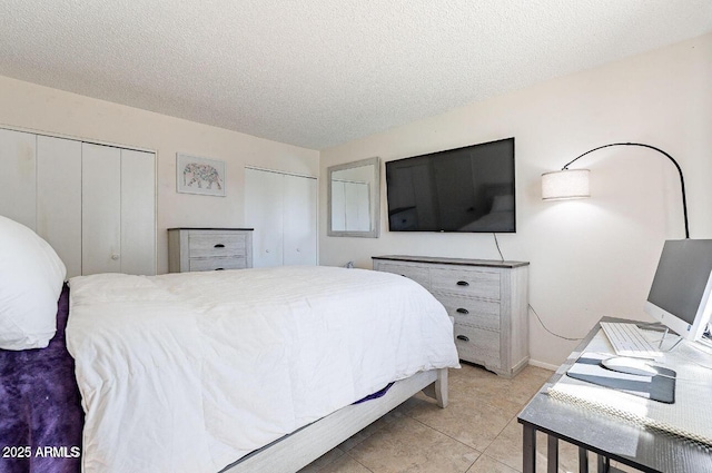 bedroom featuring a textured ceiling, two closets, light tile patterned floors, and baseboards