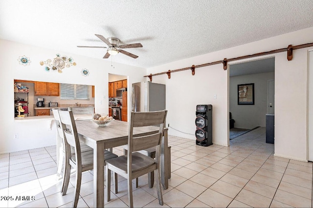 dining room with a barn door, ceiling fan, light tile patterned floors, and a textured ceiling