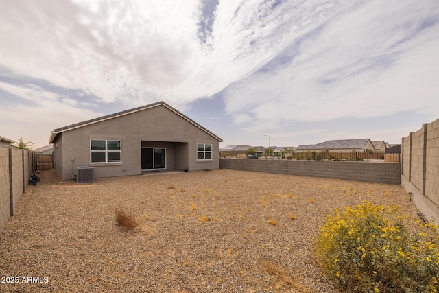 rear view of house with a fenced backyard, central AC, and stucco siding