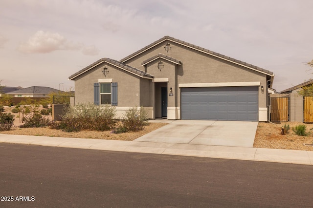 view of front facade with fence, driveway, an attached garage, stucco siding, and a tiled roof