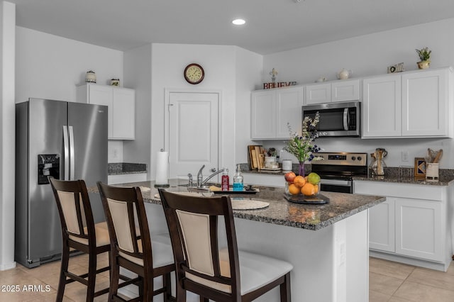 kitchen with dark stone counters, a kitchen bar, light tile patterned floors, appliances with stainless steel finishes, and white cabinetry