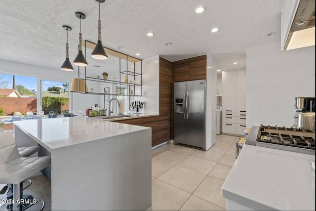 kitchen featuring a kitchen breakfast bar, a peninsula, light countertops, stainless steel refrigerator with ice dispenser, and a sink
