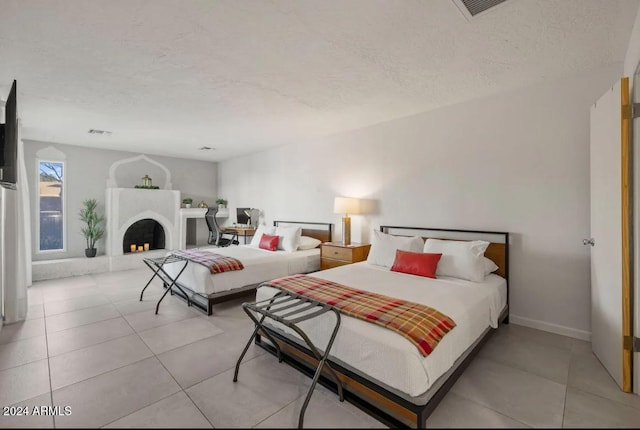 bedroom featuring visible vents, a fireplace with raised hearth, a textured ceiling, and light tile patterned floors