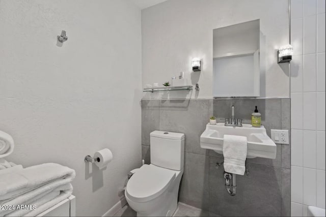 bathroom with a sink, tile walls, and toilet
