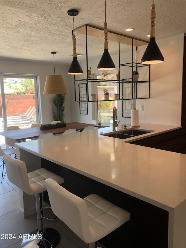 kitchen with a breakfast bar area, hanging light fixtures, a kitchen island with sink, a sink, and a textured ceiling