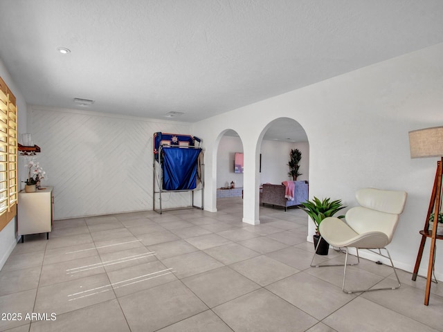 living area featuring arched walkways, a textured ceiling, visible vents, and tile patterned floors