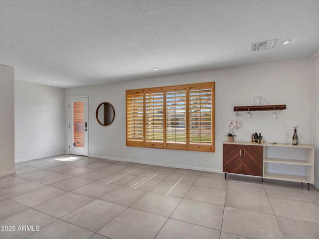empty room with light tile patterned floors, a textured ceiling, visible vents, and baseboards