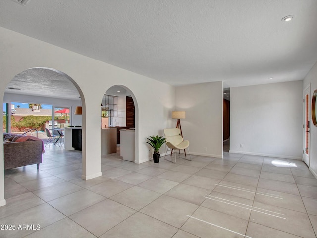 unfurnished room featuring baseboards, arched walkways, a textured ceiling, and light tile patterned flooring