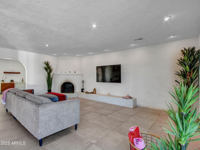living area with arched walkways, a textured ceiling, a glass covered fireplace, and recessed lighting