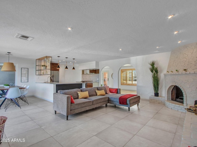living room featuring visible vents, arched walkways, a textured ceiling, a fireplace, and light tile patterned flooring