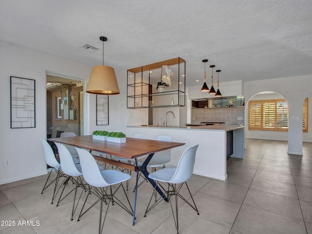 dining area featuring light tile patterned floors, baseboards, visible vents, arched walkways, and a textured ceiling