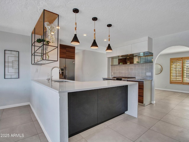 kitchen with tasteful backsplash, light countertops, modern cabinets, stainless steel fridge, and a peninsula