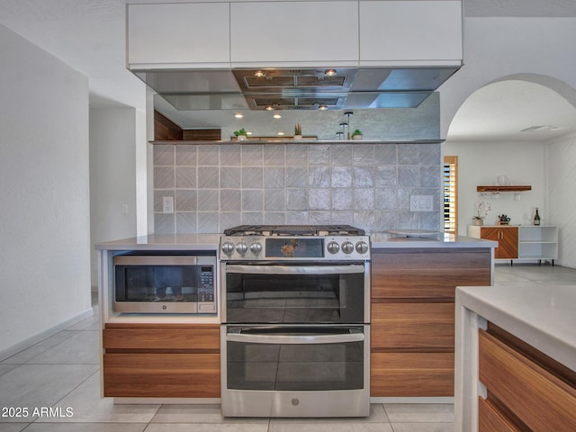 kitchen with arched walkways, modern cabinets, stainless steel appliances, backsplash, and light tile patterned flooring