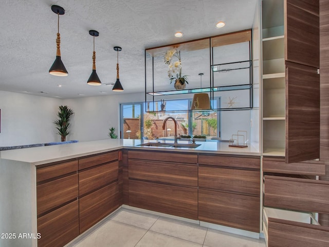 kitchen featuring light tile patterned floors, brown cabinets, a textured ceiling, pendant lighting, and a sink
