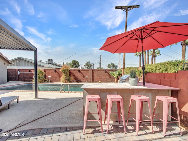 view of patio / terrace with a fenced in pool, a fenced backyard, outdoor dry bar, a grill, and exterior kitchen