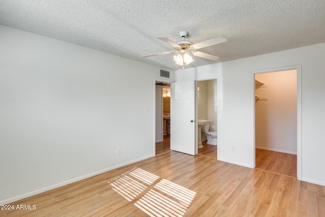 unfurnished bedroom featuring light wood-type flooring, a walk in closet, ceiling fan, connected bathroom, and a closet