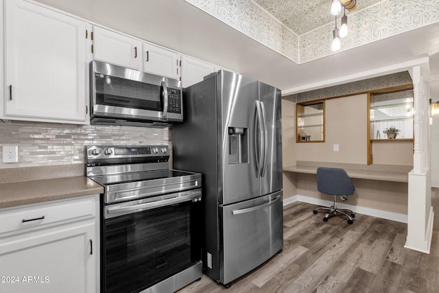 kitchen featuring white cabinets, light hardwood / wood-style flooring, built in desk, appliances with stainless steel finishes, and tasteful backsplash