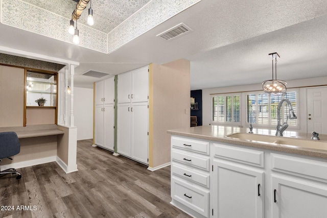 kitchen with pendant lighting, white cabinets, sink, a textured ceiling, and wood-type flooring