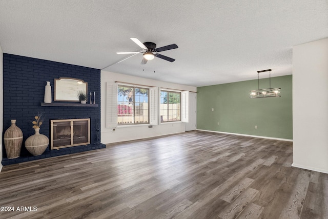 unfurnished living room with ceiling fan, dark hardwood / wood-style flooring, a textured ceiling, and a brick fireplace