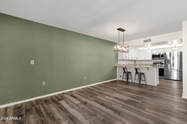 kitchen featuring white cabinets, appliances with stainless steel finishes, decorative light fixtures, dark hardwood / wood-style flooring, and kitchen peninsula