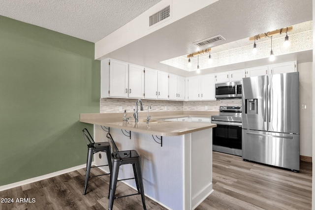 kitchen featuring kitchen peninsula, a textured ceiling, stainless steel appliances, light hardwood / wood-style floors, and white cabinetry