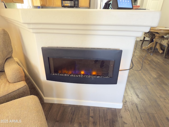 interior details with a glass covered fireplace, wood finished floors, baseboards, and black microwave