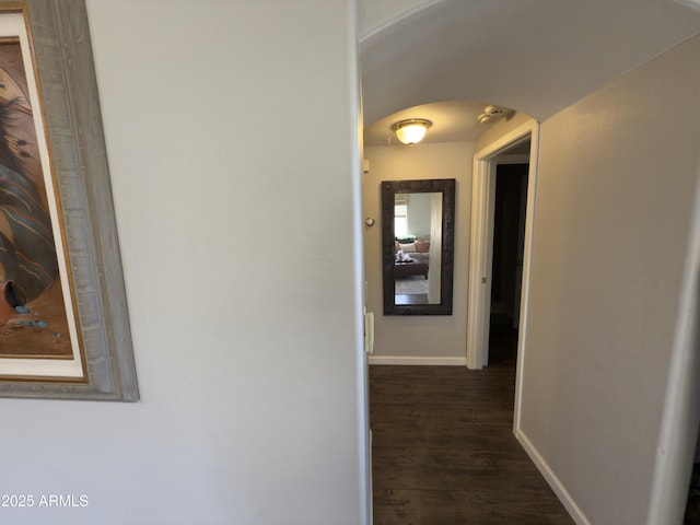 hallway with arched walkways, baseboards, and dark wood-style flooring